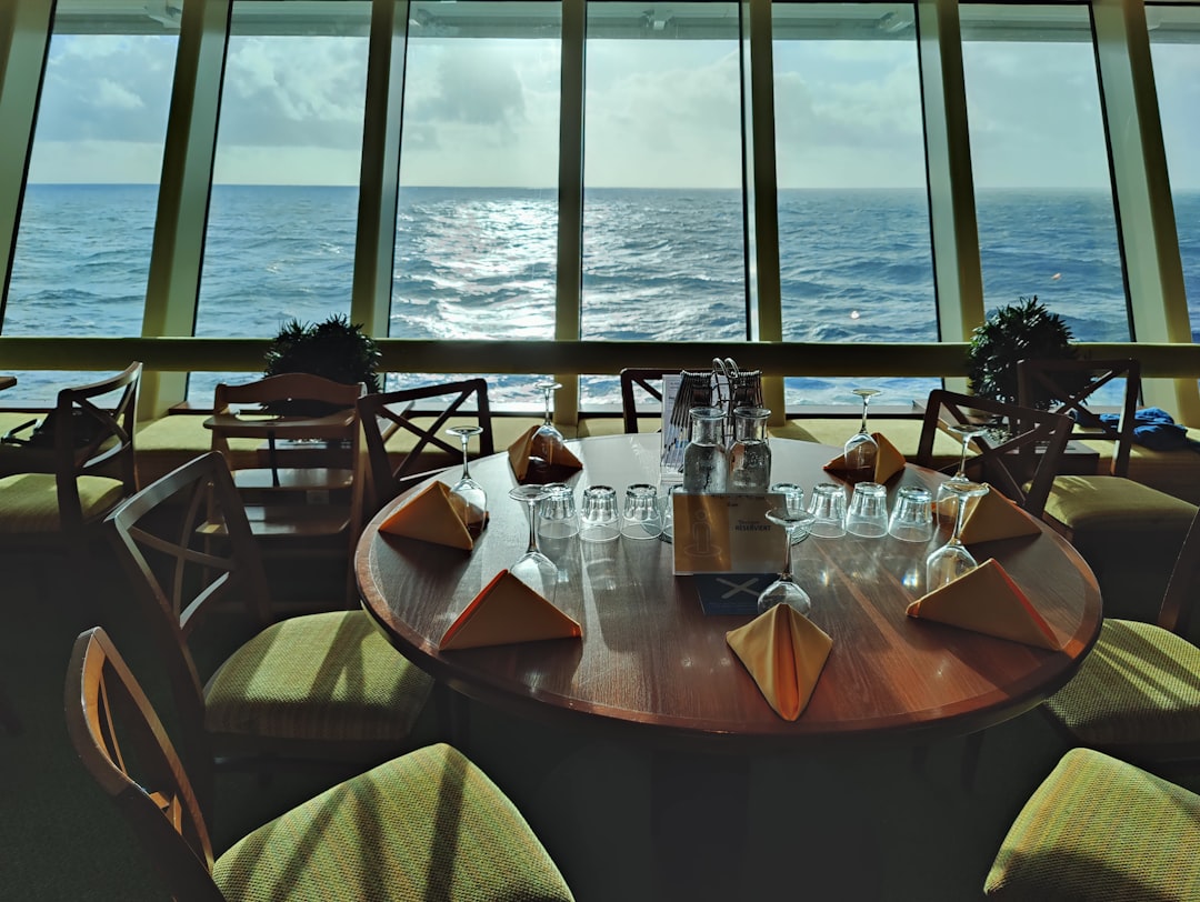 White-tablecloth dinner table on a ship's open deck at golden hour, wine glasses catching low sun over open sea