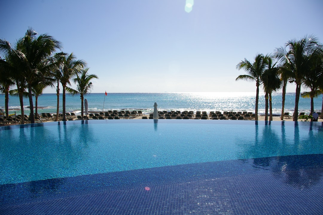 Calm resort infinity pool at mid-morning with an empty float, two loungers, and turquoise sea beyond.