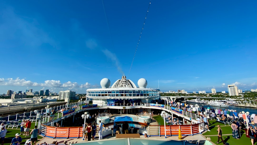 Small figures walking a Caribbean pier beneath the towering white hull of a massive cruise ship in afternoon light
